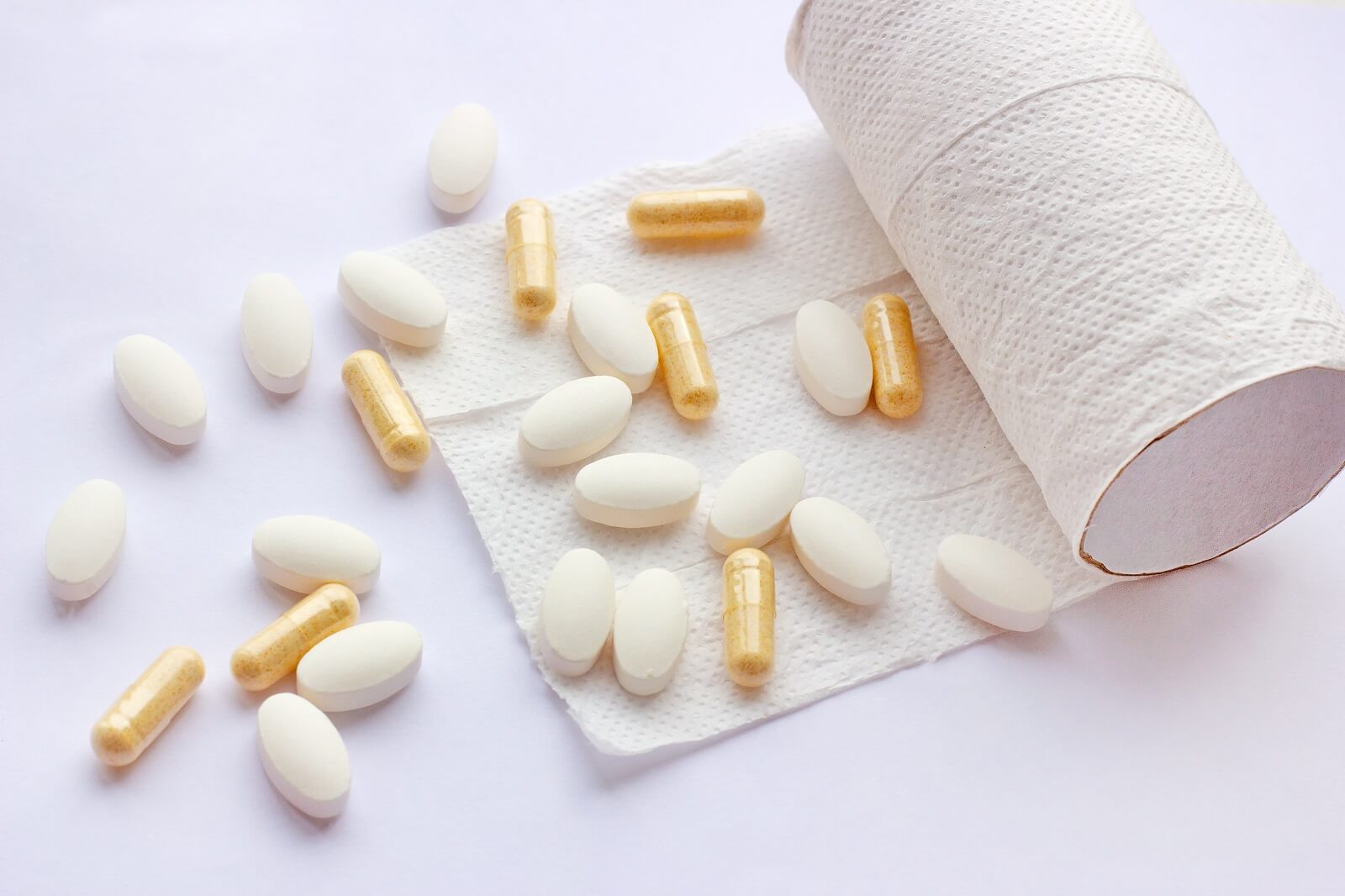 Pills, capsules and tablets with toilet paper on light background. Pharmacy and medicine concept.