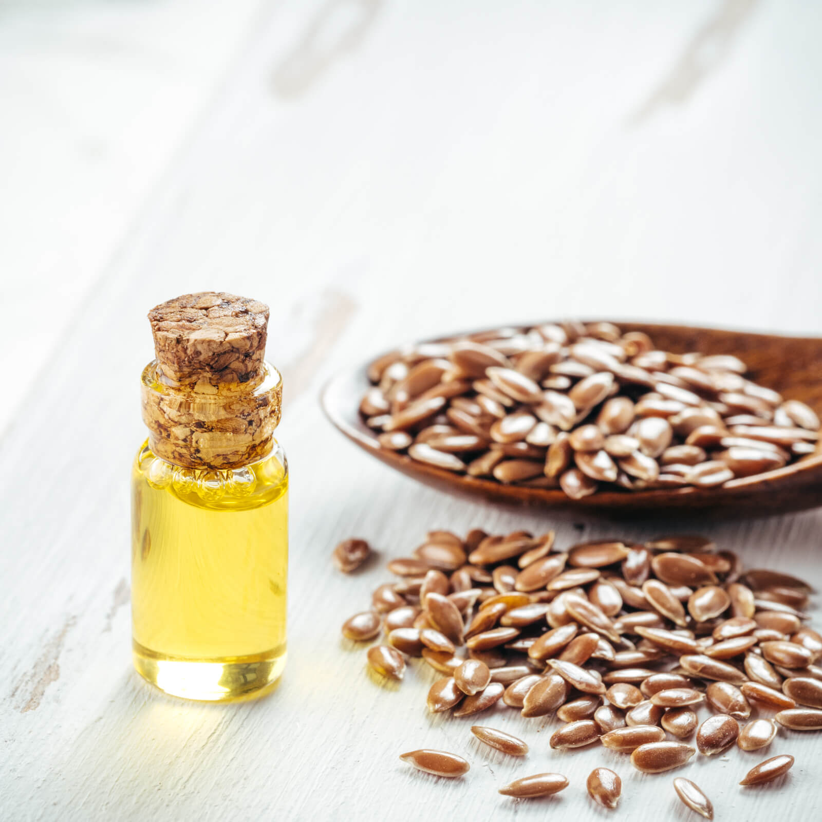 Brown flax seeds in spoon and flaxseed oil in glass bottle on white wooden background.
