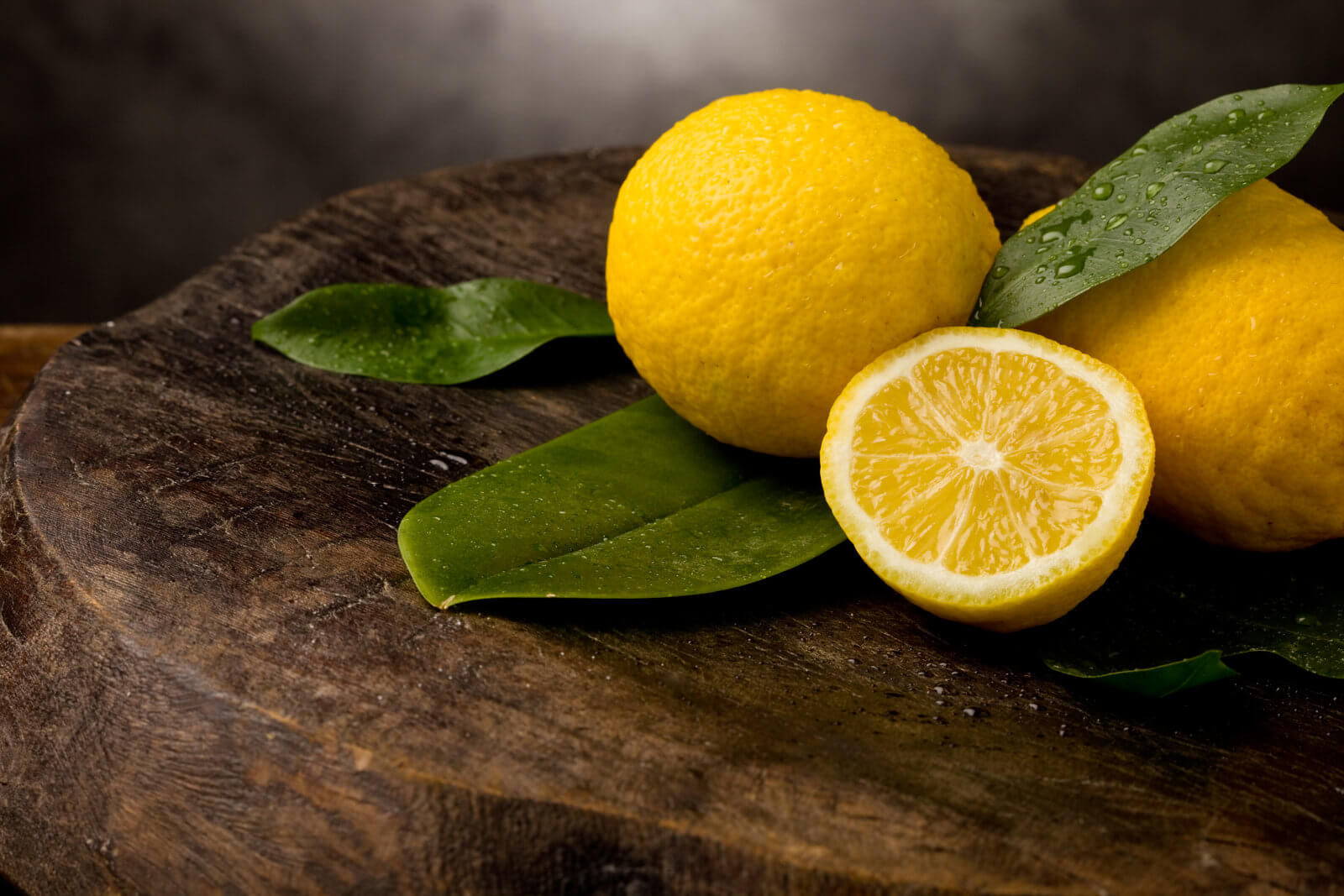 Fresh yellow lemons with leaves and water drops on a wooden table