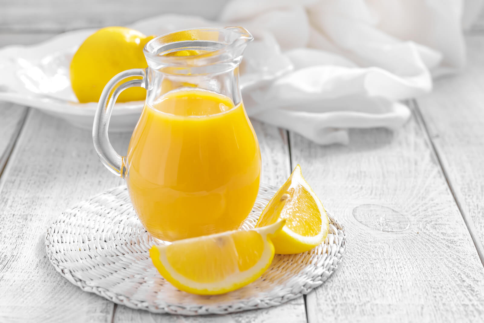 A glass pitcher with lemon juice with cut lemons beside it. 