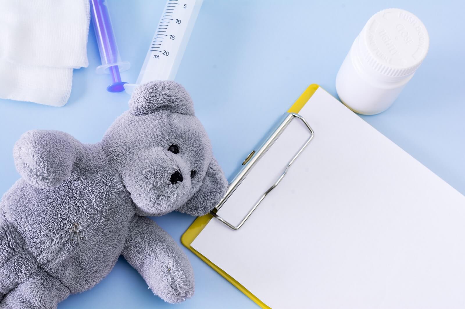 Medical conceptual picture with pills, teddy bear, injection, gauze, bottle, empty clipboard sheet.