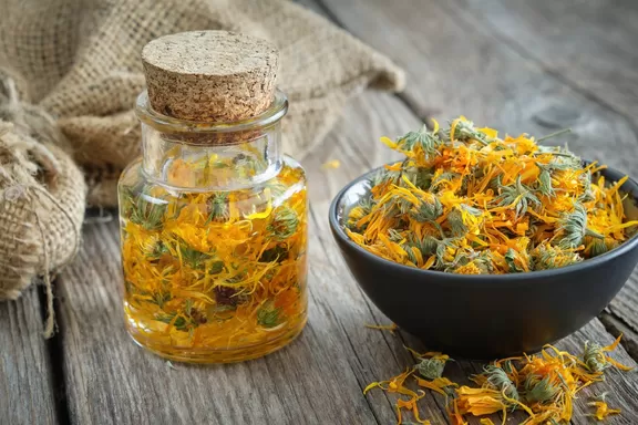 Bottles of calendula infusion or oil, healthy marigold flowers in bowl and canvas sack on background. Herbal medicine.