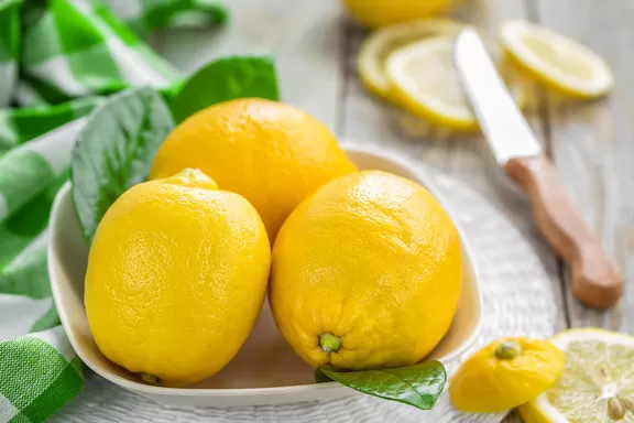 Lemons (Citrus limon) in a bowl with green leaves.