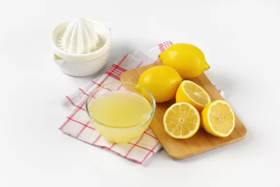 Lemons on a wooden cutting board with lemon juice and a hand juice press