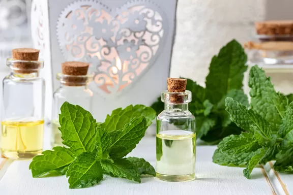 A bottle of essential oil with fresh peppermint leaves on a table.