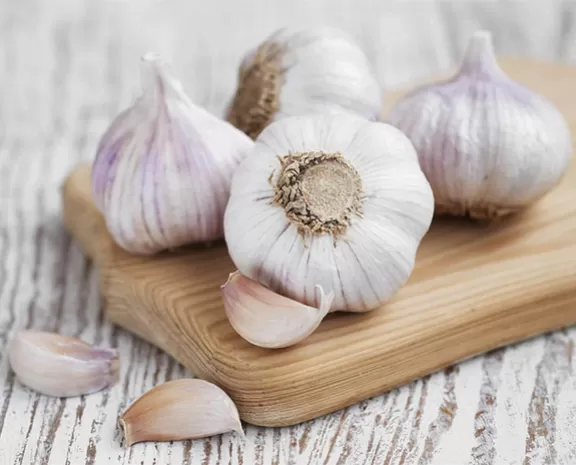 Garlic bulbs on a wooden board with garlic cloves around it.